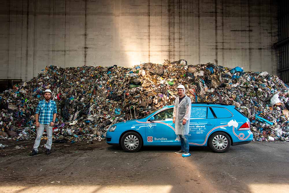 Wiebe Wakker bezoekt een duurzaamheids initiatief Wiebe Wakker met zijn auto samen voor een berg afval, met een medewerker van een afval recycling fabriek waar Wiebe op bezoek is.